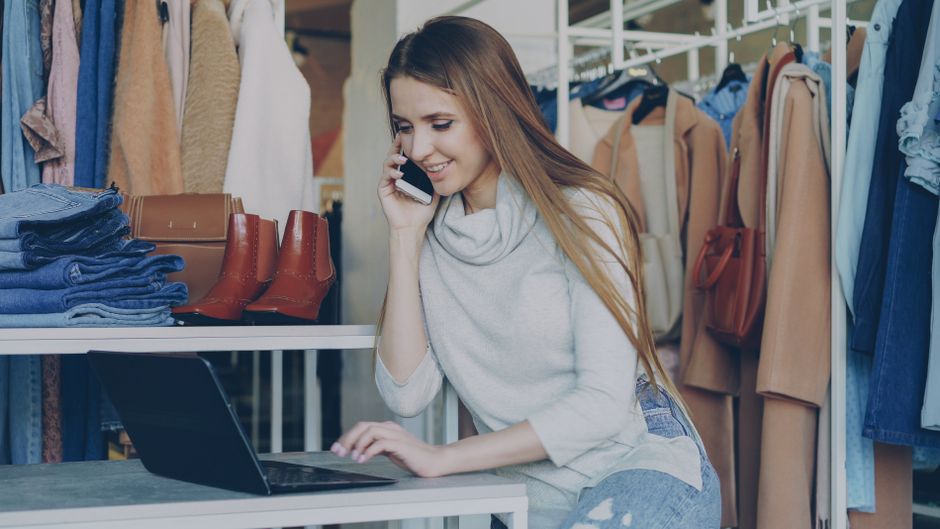 Comerciante atendiendo una llamada junto a su computadora y un catálogo de ropa